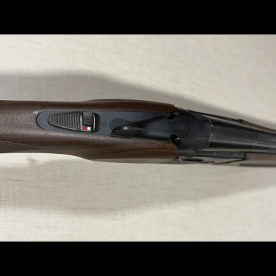 Espingarda de canos duplos com coronha madeira castanha e mecanismos metálicos pretos.