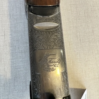 Detalhe de arma de fogo com parte metálica gravada e madeira castanha