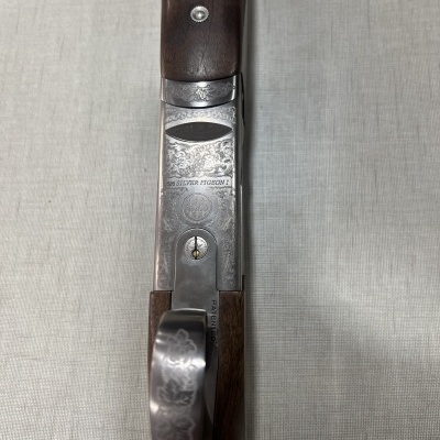 Espingarda com empunhadura em madeira castanha e corpo metálico gravado sobre tecido cinzento