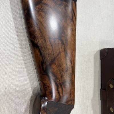 Coronha de espingarda em madeira castanha com bolsa de couro castanho ao lado