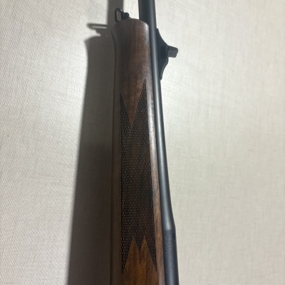 Rifle com coronha em madeira castanha e cano preto encostado a parede branca