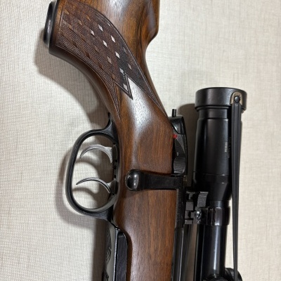 carabina de madeira castanha com mira telescópica preta sobre fundo bege