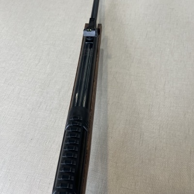 Espingarda com empunhadura preta e corpo em madeira escura sobre tecido bege