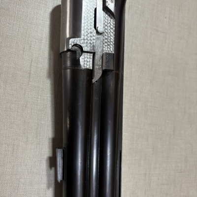 Cano metálico preto e prata de arma de fogo com gravação, sobre fundo bege texturizado