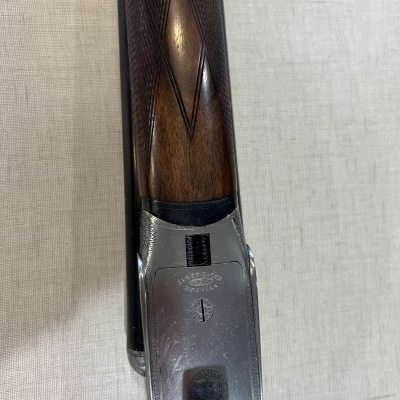 Arma de caça com cabo em madeira castanha e metal prateado sobre tecido bege