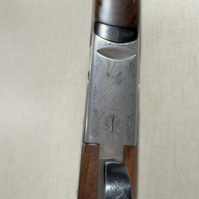 Espingarda com detalhes em madeira, metal gravado e inscrições visíveis sobre tecido bege.