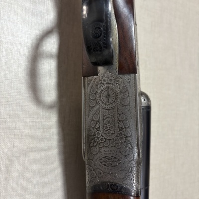 Parte superior de arma de fogo em madeira escura e metal com gravações florais detalhadas