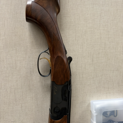 Espingarda de caça em madeira castanha com gatilho dourado e caixa de plástico BERETTA ao lado