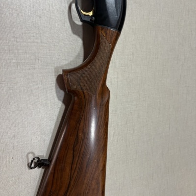 Punho de espingarda em madeira castanha com gatilho dourado e corpo metálico preto