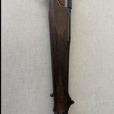 Rifle com coronha de madeira escura e detalhes metálicos em fundo neutro