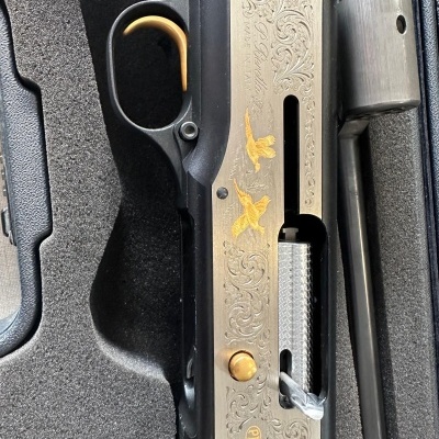 Espingarda de caça com decoração dourada e cabo de madeira num estojo de espuma.