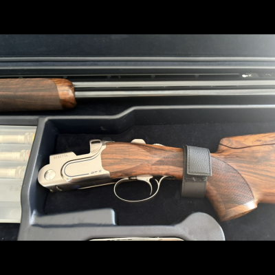 Espingarda de cano duplo desmontada com madeira castanha e metal prateado na caixa preta.