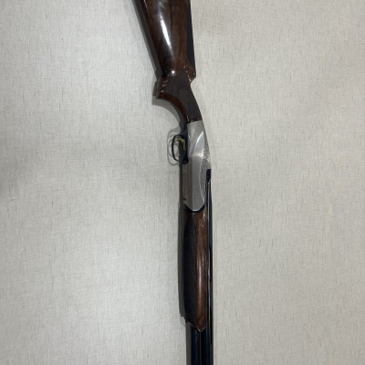 Espingarda de cano duplo com madeira castanha e metal prateado, em fundo neutro