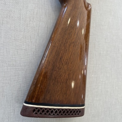 Coronha de arma de madeira polida com borracha na extremidade, sobre tecido cinza