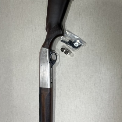 Espingarda com coronha em madeira castanha e partes em metal prateado sobre fundo claro