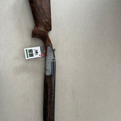 Espingarda com coronha em madeira castanha e canos pretos sobre fundo bege