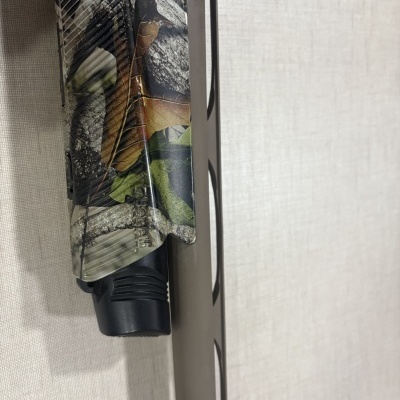 Peça de arma camuflada com padrão de folhas e ramos e detalhe em plástico preto