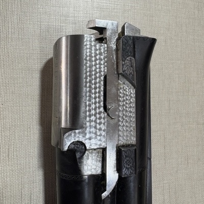 Parte superior de arma de fogo metálica com detalhes gravados em negro e metal polido