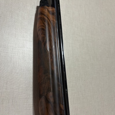 Parte de uma espingarda em madeira e metal preto encostada numa parede clara.