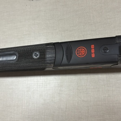 Parte de arma preta com punho texturizado e inscrições vermelhas