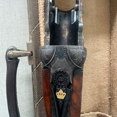 Parte superior de arma de fogo com detalhes metálicos e símbolo de coroa dourada