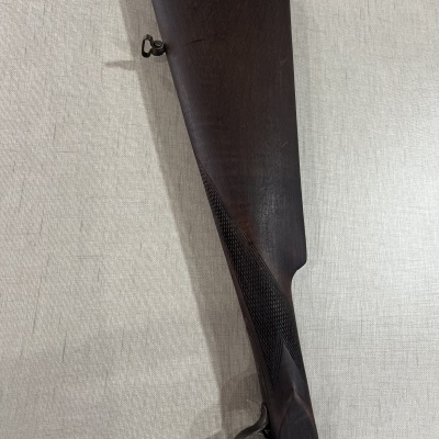 Coronha de madeira escura para arma de fogo com textura geométrica perto do punho em fundo claro