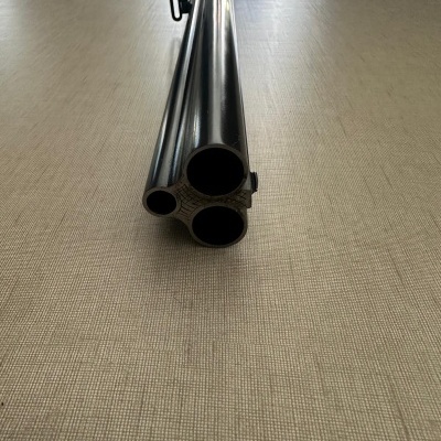 Espingarda de três canos paralelos em metal preto sobre mesa clara.