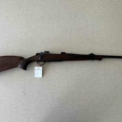 Rifle de madeira escura com cano metálico longo e luneta em superfície bege