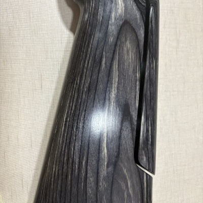 Coronha de madeira escura para arma, com base de borracha preta sobre tecido bege.