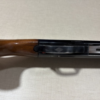 Parte de arma com coronha de madeira castanha e mecanismo metálico preto.