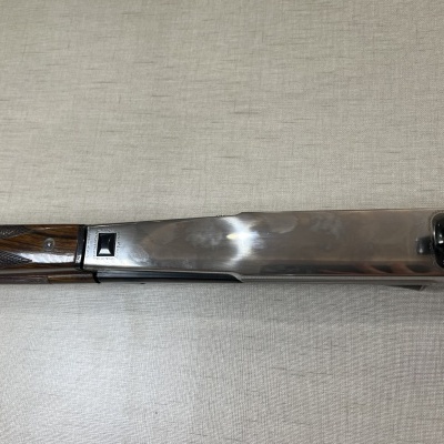 Espingarda com madeira escura e metal prateado sobre tecido bege.