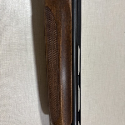 Espingarda com cano metálico preto e coronha em madeira castanha encostada numa parede clara