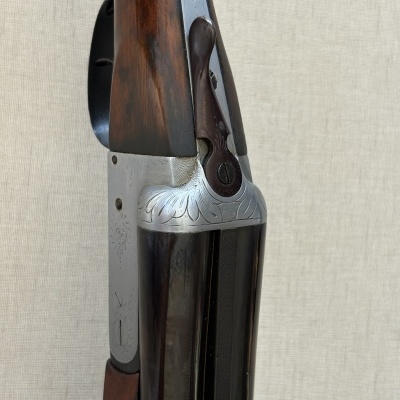 Detalhe de arma de fogo de caça em madeira e metal com gravações decorativas.