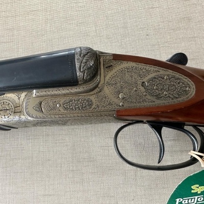 Espingarda de canos sobrepostos com detalhes gravados em metal prateado e madeira castanha