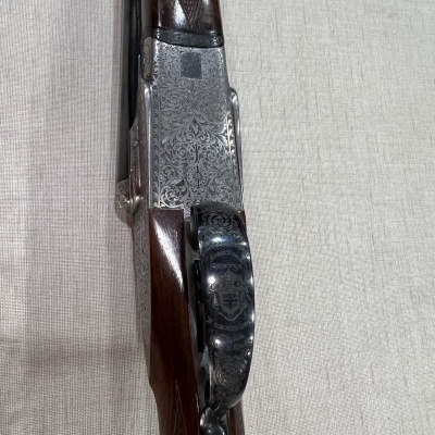 Parte central de espingarda com madeira castanha e metal gravado em padrão floral sobre tecido bege