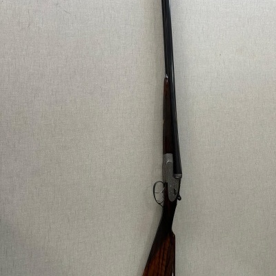Espingarda de cano duplo e coronha de madeira escura encostada numa parede clara