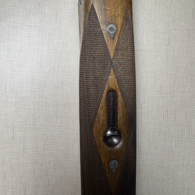 Empunhadura de arma de fogo em madeira castanha com detalhes metálicos e textura quadriculada.