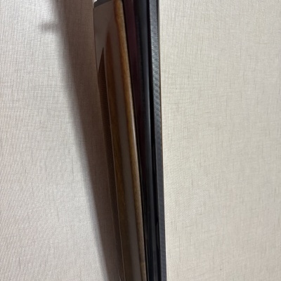 Espingarda com coronha em madeira e cano preto encostada numa parede cinza clara