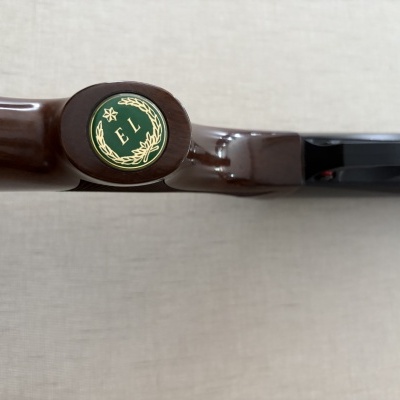 Detalhe do cabo de uma arma de fogo com botão verde com as letras E L.