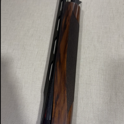 Parte superior de uma espingarda com madeira escura e detalhes metálicos.