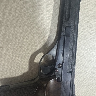 Revólver metálico preto com cabo de madeira escura e inscrições visíveis