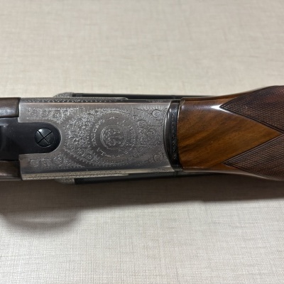 Espingarda com coronha em madeira castanha e corpo metálico gravado.
