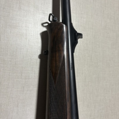 Espingarda com coronha de madeira escura e cano longo preto contra parede clara
