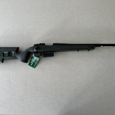 Espingarda de caça preta com etiqueta verde sobre superfície cinzenta