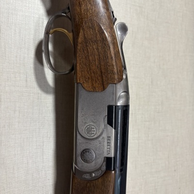 Espingarda com cabo de madeira castanha e detalhes metálicos prateados, gatilho dourado e texto BERETTA