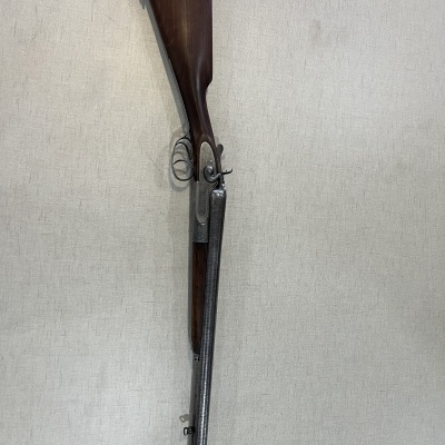 Espingarda de canos duplos com coronha em madeira contra parede bege.