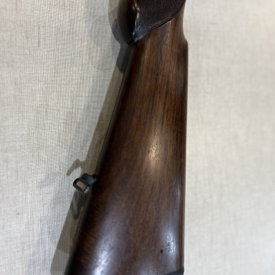 Arma de madeira castanha escura com texturas e entalhe, junto a uma superfície bege