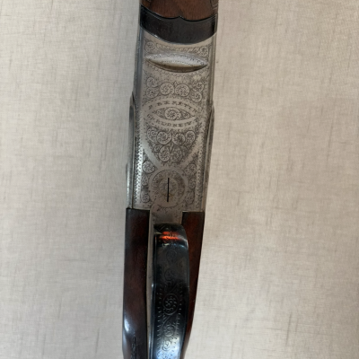 Espingarda de caça em madeira e metal com gravações decorativas e texto gravado.