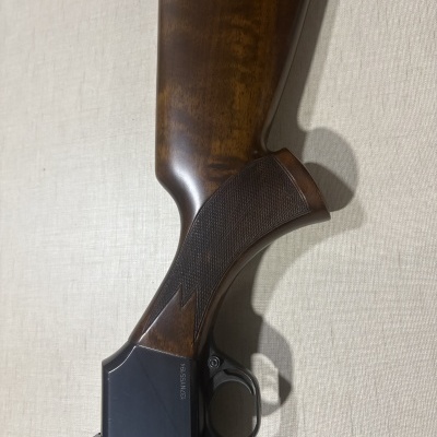 Coronha de espingarda em madeira castanha com textura e parte metálica preta com número gravado.