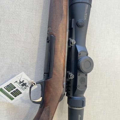 Espingarda com coronha de madeira e mira telescópica preta sobre fundo cinzento